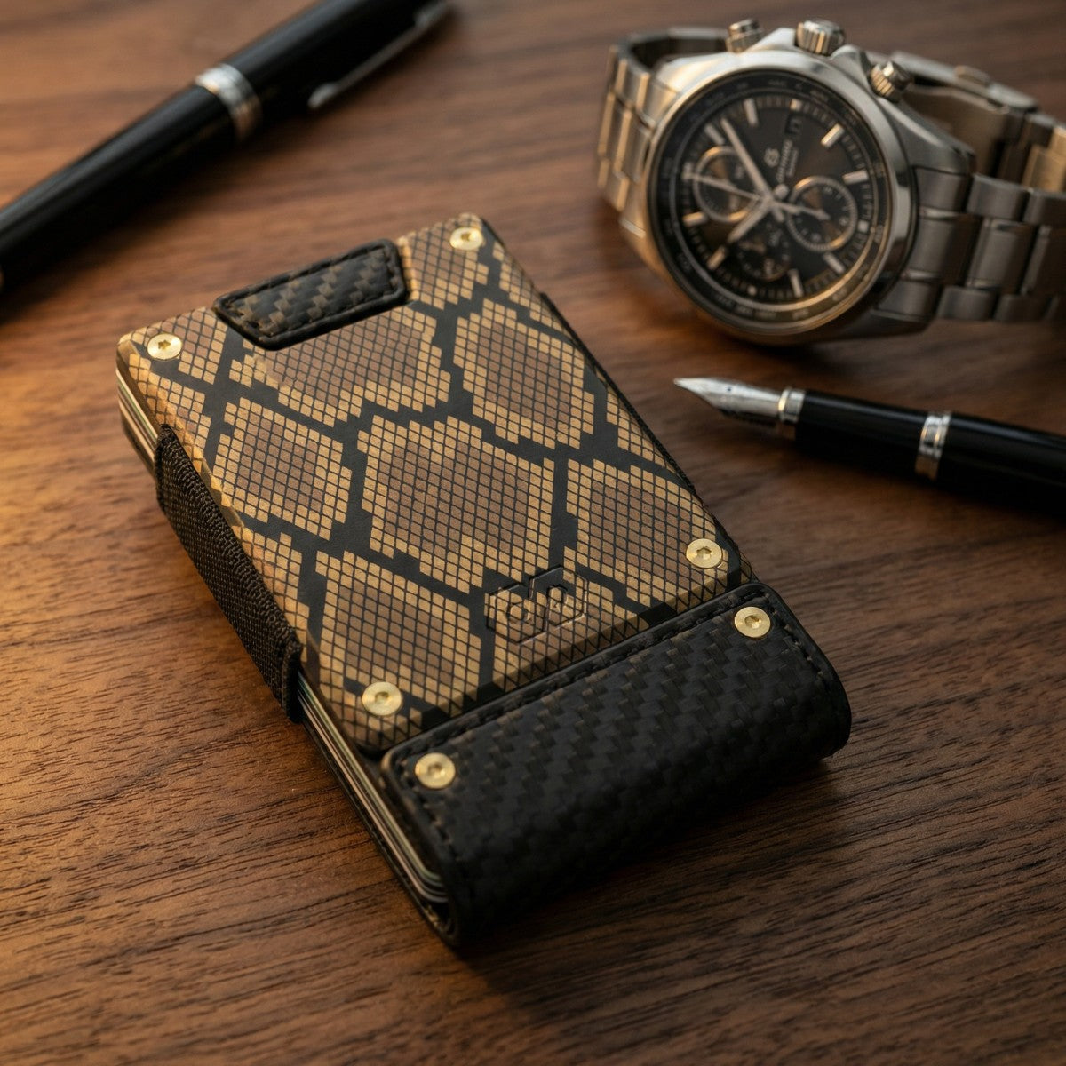 Snake-print and carbon fiber minimalist wallet with gold rivets, displayed beside a chronograph watch and fountain pens on wa