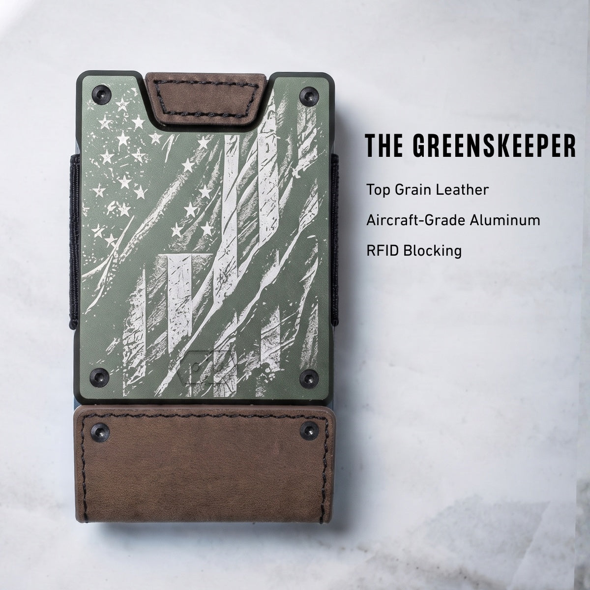 A slim wallet-style card holder with a distressed American flag design in muted green and white, with brown leather trim and a matching brown leather base. Text on the right reads 'THE GREENSKEEPER' with material and feature callouts.