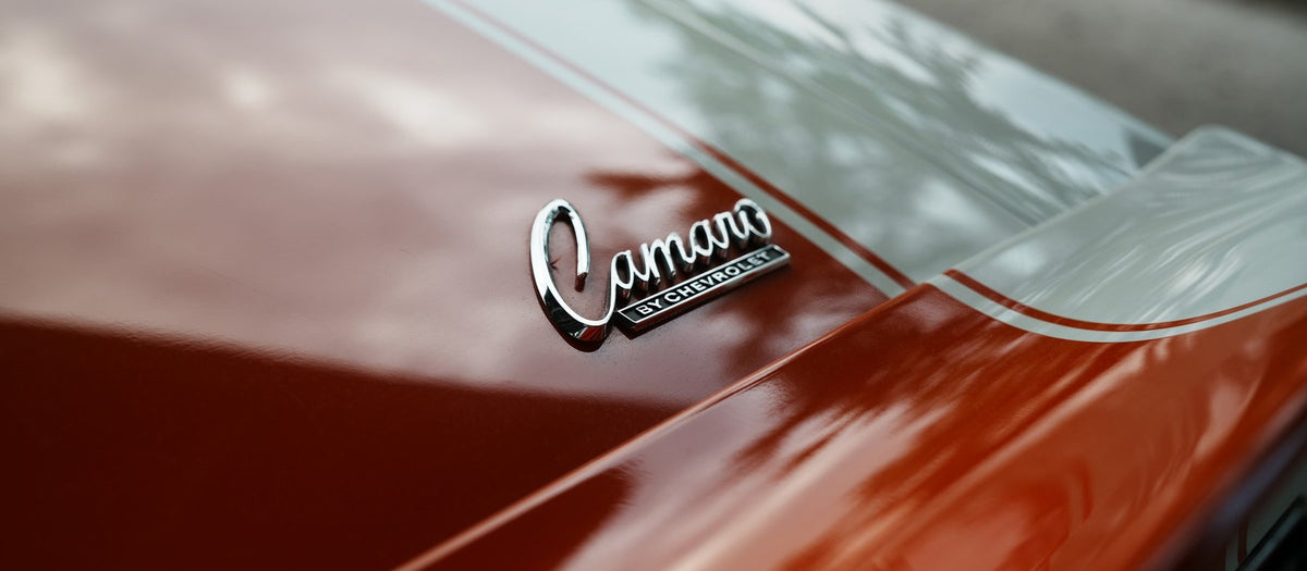 Chrome Camaro by Chevrolet script badge on the Hugger Orange cowl