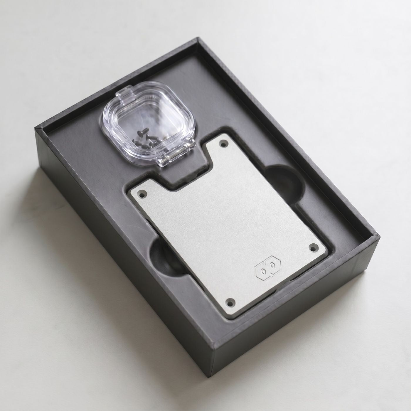 Wallet Plate Upgrade kit unboxed in dark grey foam tray, showing silver metal plate and small hardware accessory case.
