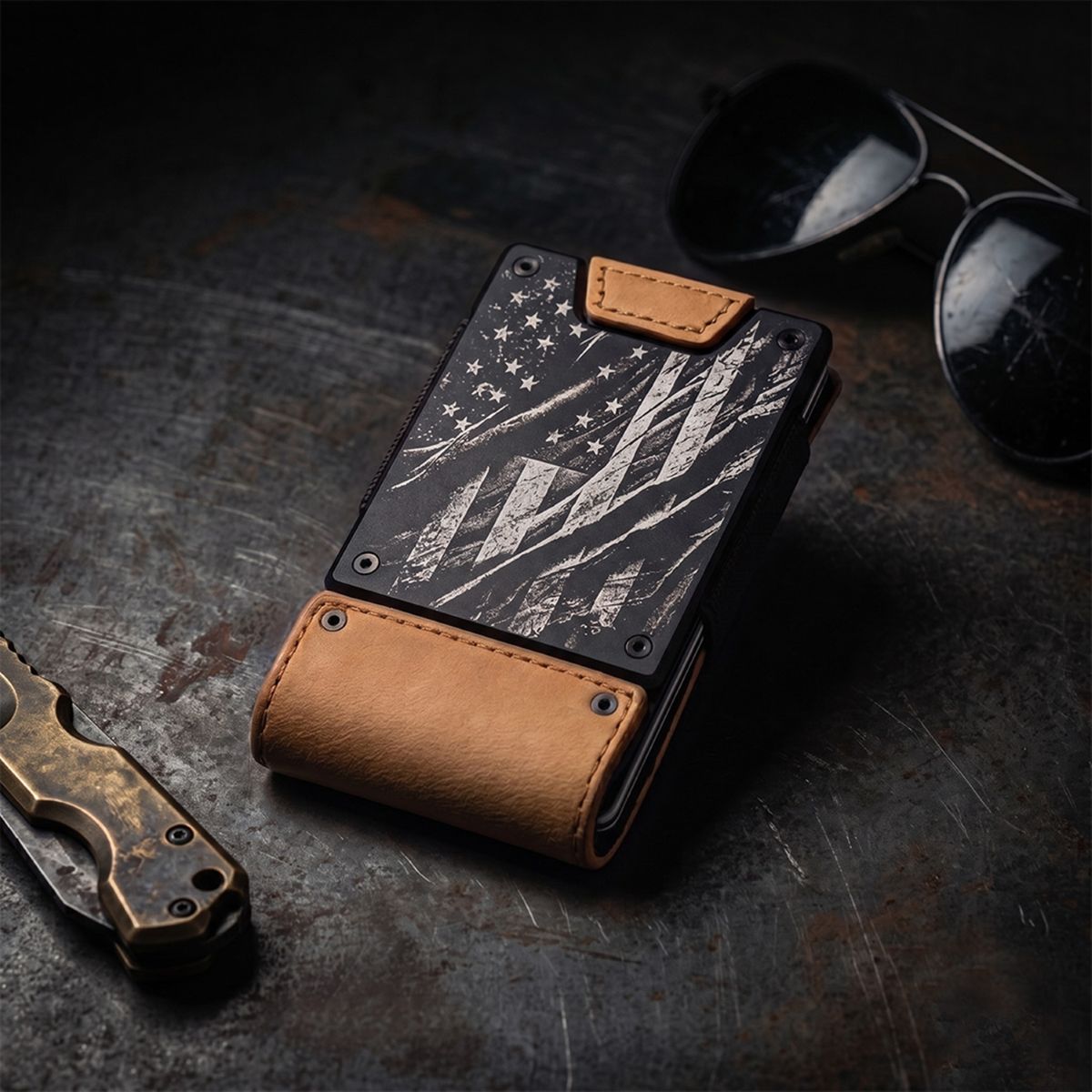 A slim black and tan leather wallet with a distressed American flag design, displayed on a dark textured surface next to sunglasses and a folding knife.