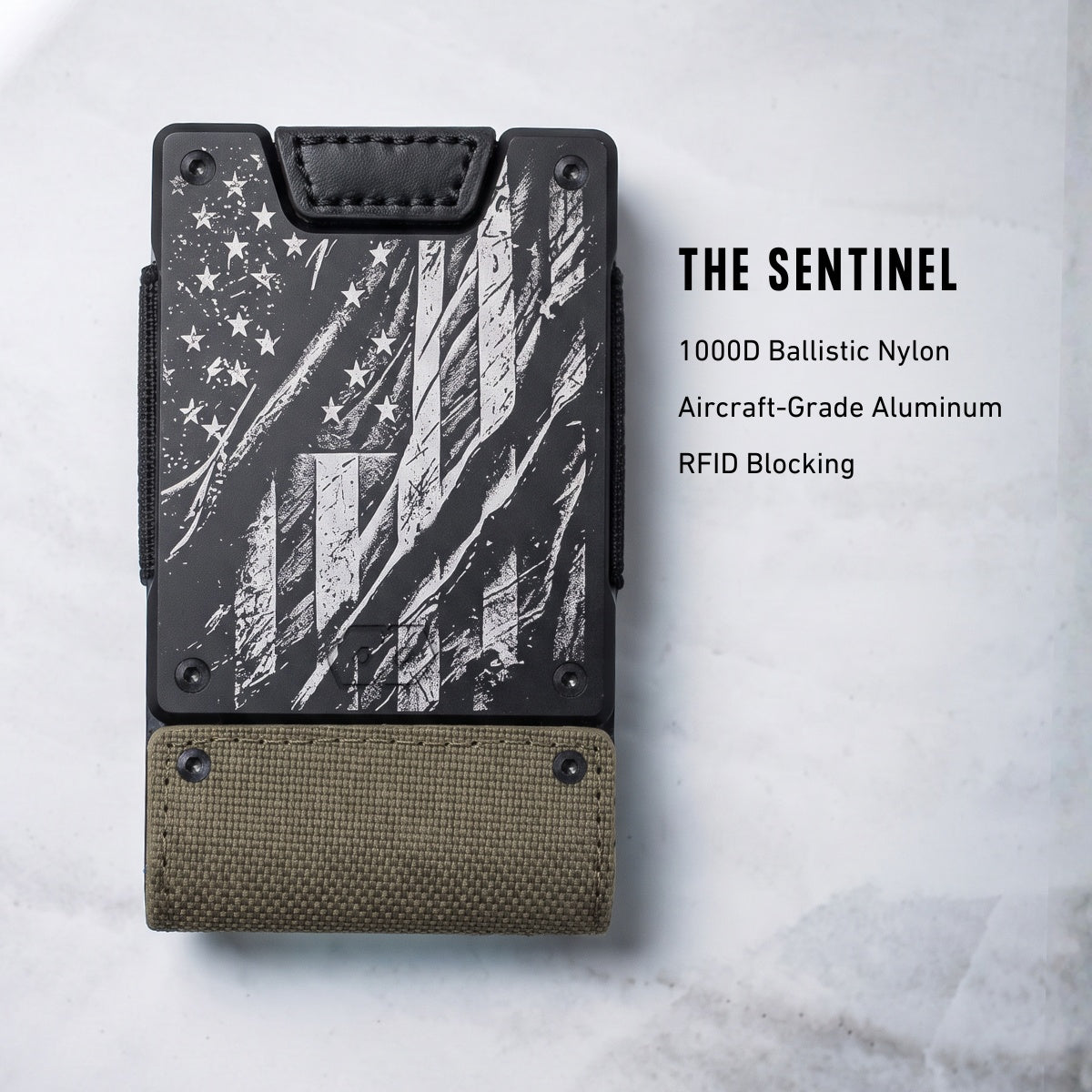 A slim vertical wallet-style card holder shown on a light marble background with text reading 'THE SENTINEL' and material callouts. The product has a black distressed American flag print on the upper section and an olive drab fabric section at the bottom, with black side hardware.