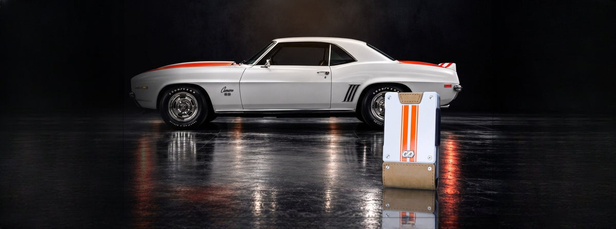 1969 Camaro Z10 in a dark studio beside a PROOF wallet with orange racing stripes